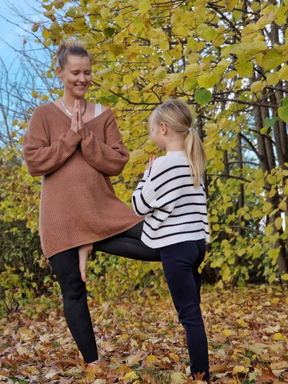 Familienyoga und Kinderyoga Lehrerin Mandy steht gemeinsam mit ihrer Tochter in einer Yogapose in herbstlicher Umgebung
